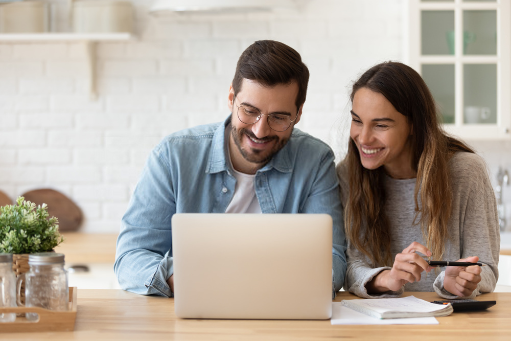 Manter saúde financeira da empresa: um homem e um mulher sorriem ao olhar para a tela do notebook em cima da mesa