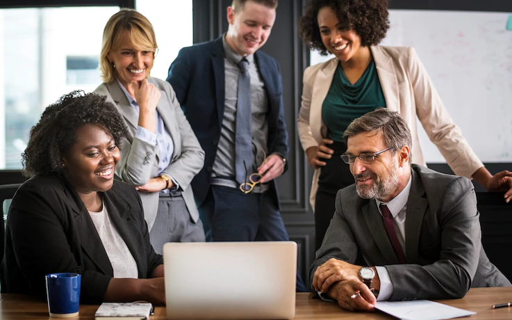 As principais vantagens do fomento mercantil: Grupo de cinco empresários (3 mulheres e 2 homens) sorriem ao olhar para um notebook)